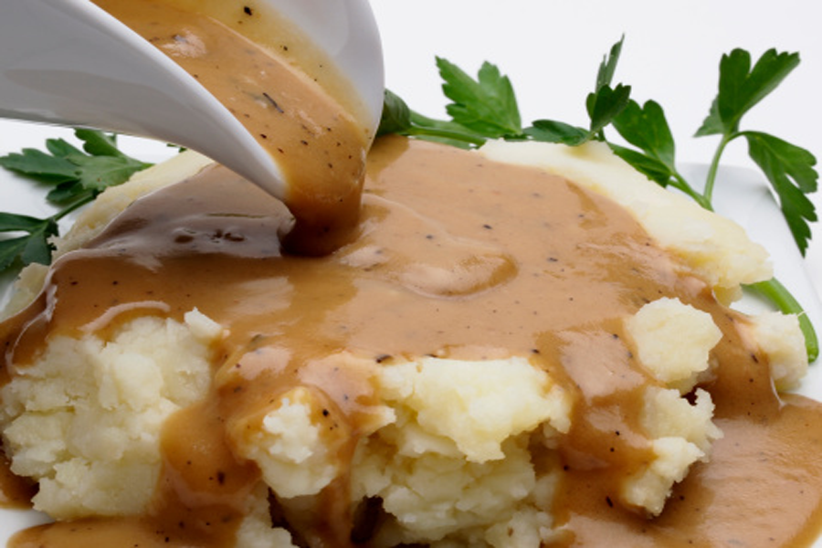 Close up of Cook's Delight Gravy in boat pouring over mashed potatoes